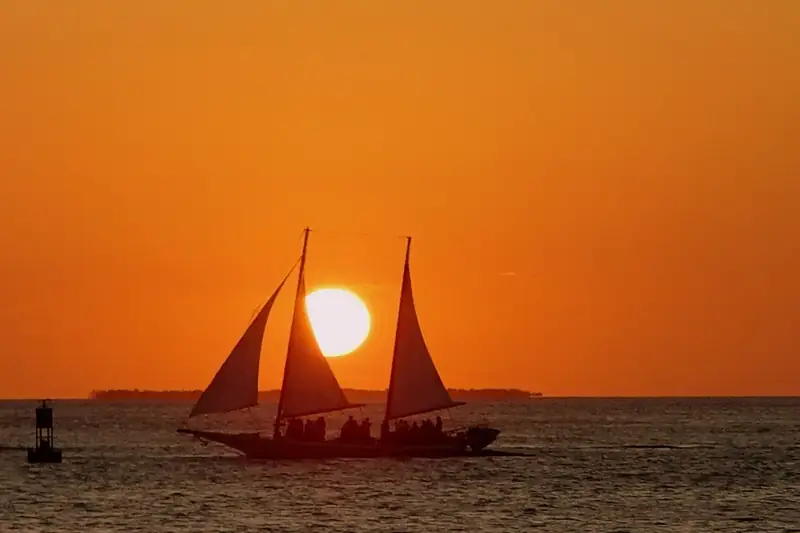 Veleiro de dois mastros contra um pôr do sol laranja